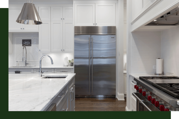 A luxury white kitchen featuring a large stainless steel refrigerator, white shaker cabinets, and a massive professional gas range cooktop.