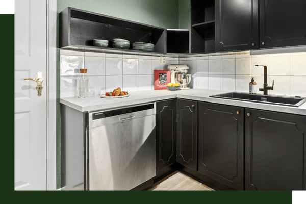 A minimalist kitchen space with matte black cabinets, white tiled walls, a stainless steel dishwasher, and under-cabinet LED strip lighting.