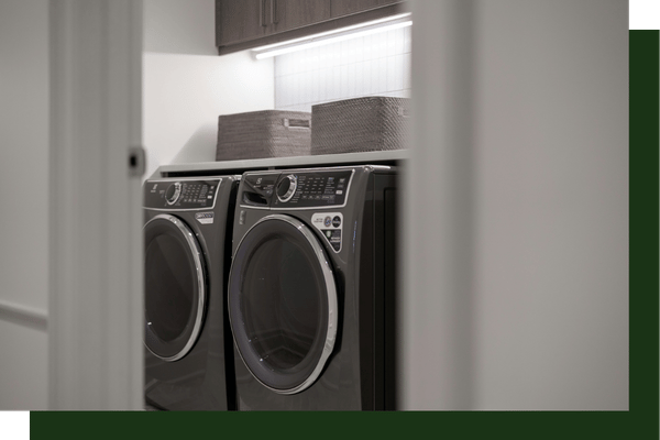 A modern laundry closet featuring a dark grey front-loading washer and dryer set neatly beneath an overhead storage shelf.