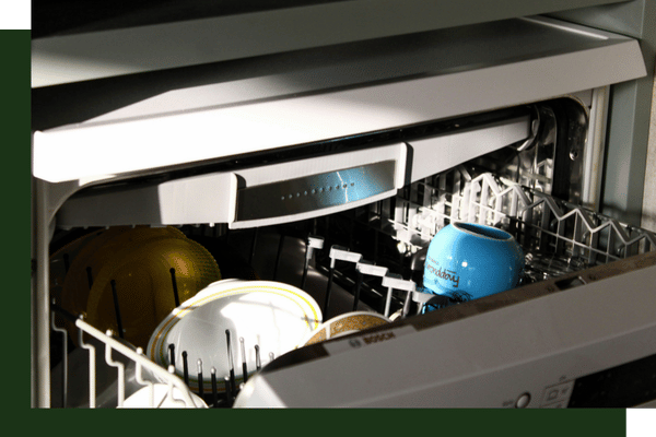 Close-up inside an open built-in dishwasher showing ceramic bowls and a bright blue mug stacked on the top rack.