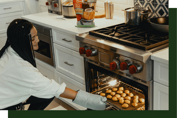 A woman wearing an oven mitt opening a professional stainless steel oven to check on freshly baked food.
