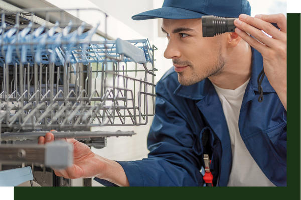 A tech using a flashlight to inspect a dishwasher