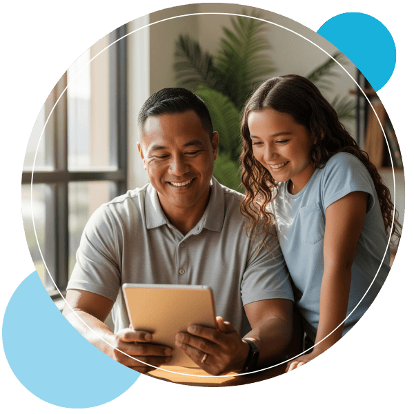 A smiling man and a smiling child look together at a tablet computer being held by the adult.