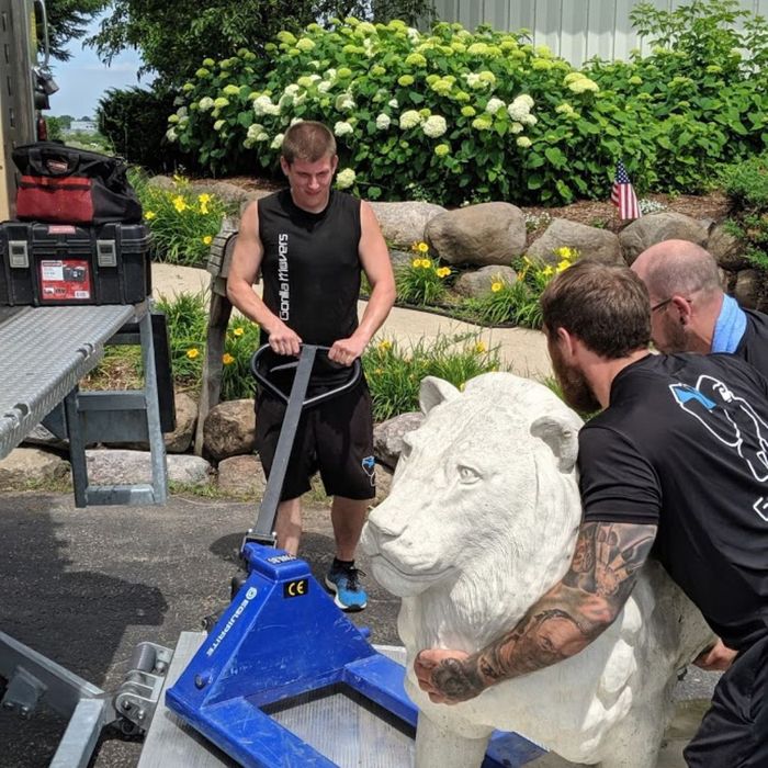 Men moving a white lion statue with pallet jack