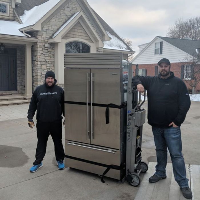 Two men moving a large refrigerator outside house