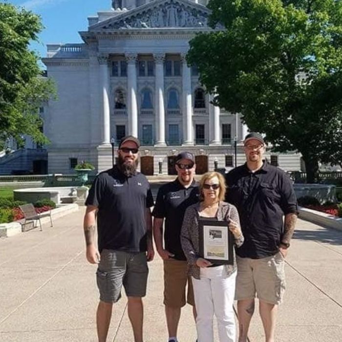 Four people holding a certificate in front of building