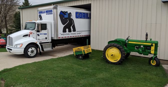 Gorilla Movers truck beside a green tractor outside building