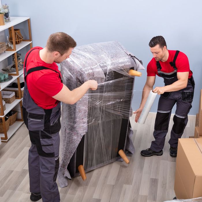 Two movers wrapping a couch. 