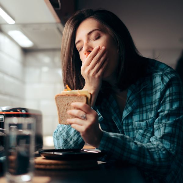 Tired woman eating a sandwich at night