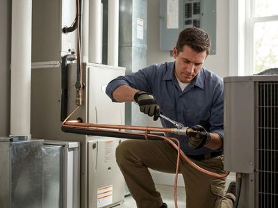A technician in work gloves kneels, carefully connecting copper pipes with a wrench during an HVAC system installation or repair. HVAC Technician Installing Copper Pipes