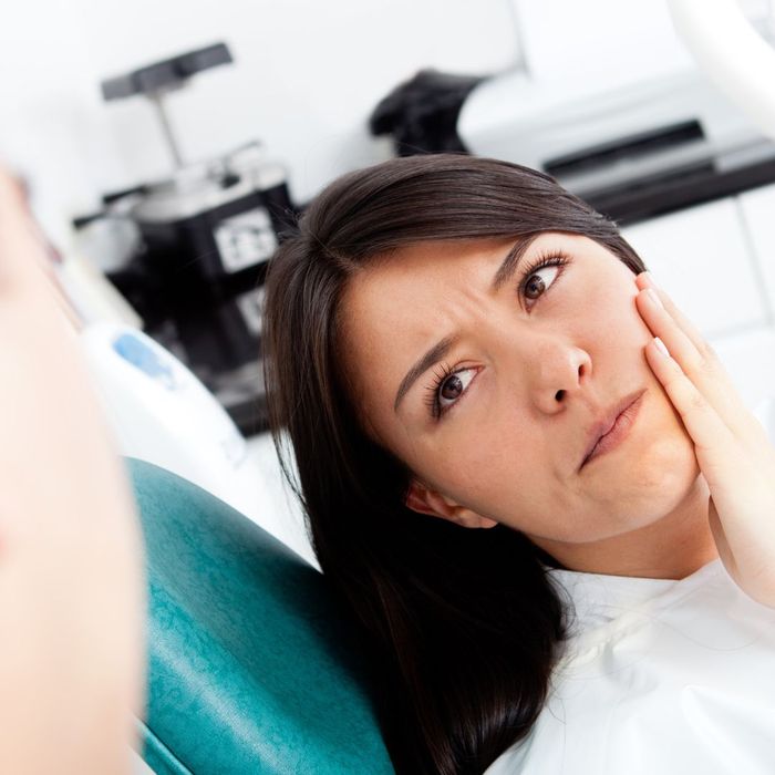 woman in dental chair holds cheek with hand Common Misconceptions About Dental Care Debunked 1.jpg