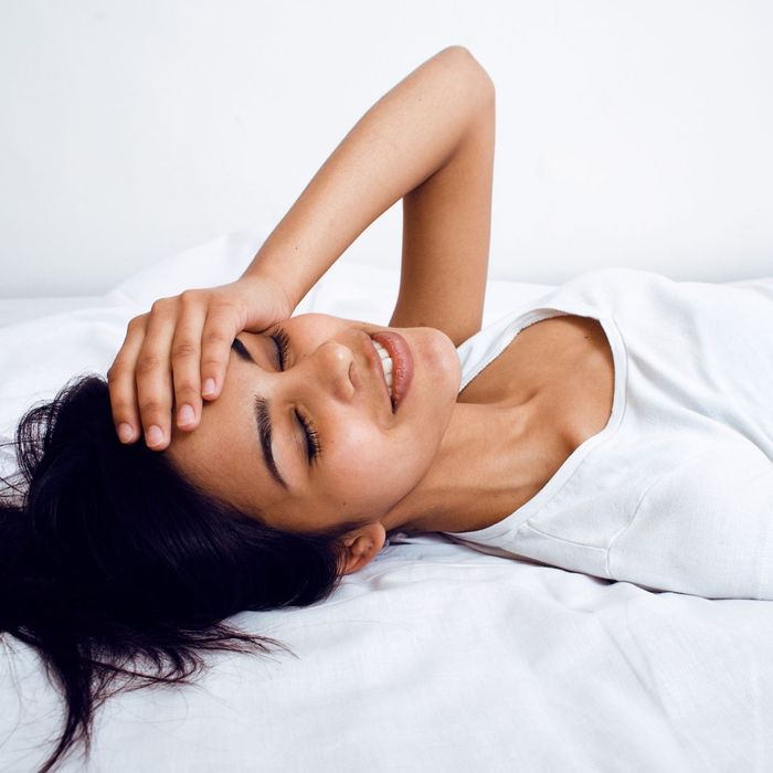 woman lays on bed holding forehead with hand How Does Stress Influence Gum Disease 3.jpg