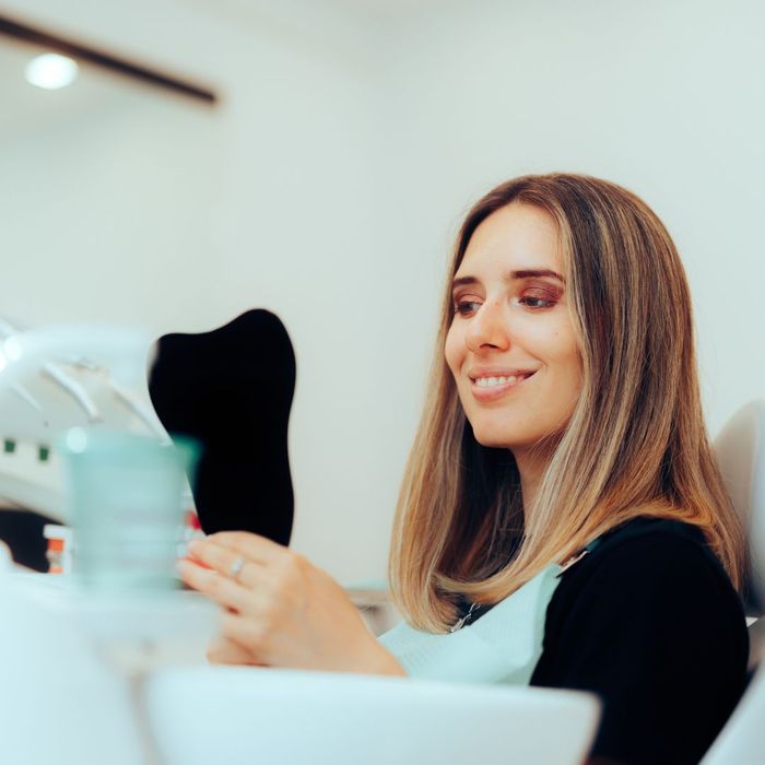 woman holds mirror to check smile Addressing Common Myths About Dental Implants 2.jpg