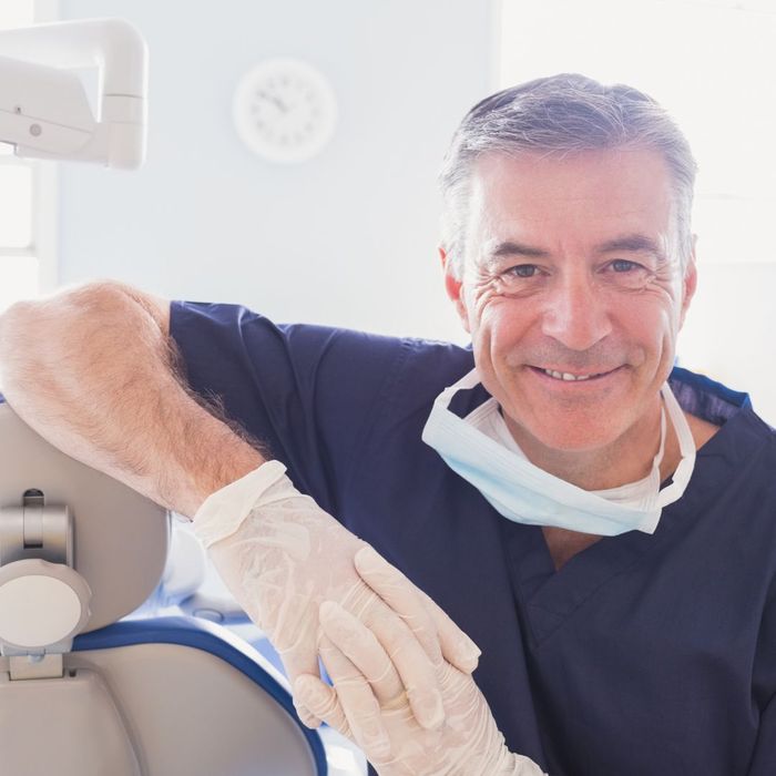 dentist leans on dental chair and smiles for photo How Can Routine Dental Check-Ups Save You Money 4.jpg