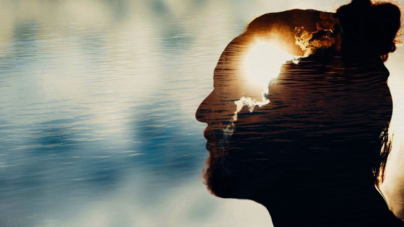 the silhouette of a man's head with clouds and the sun overlaid