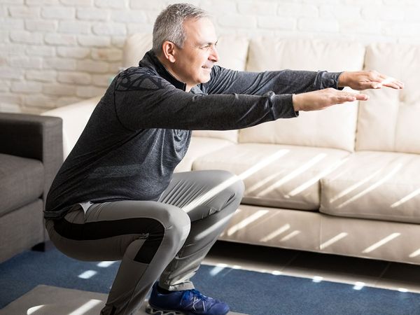 Older gentleman doing squats in workout clothing at home with an online personal trainer.