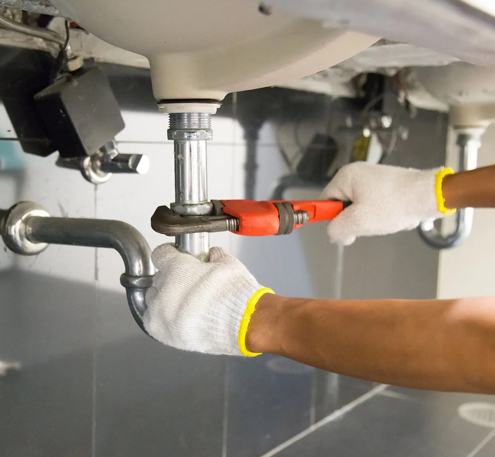 Plumber with wrench around sink pipe