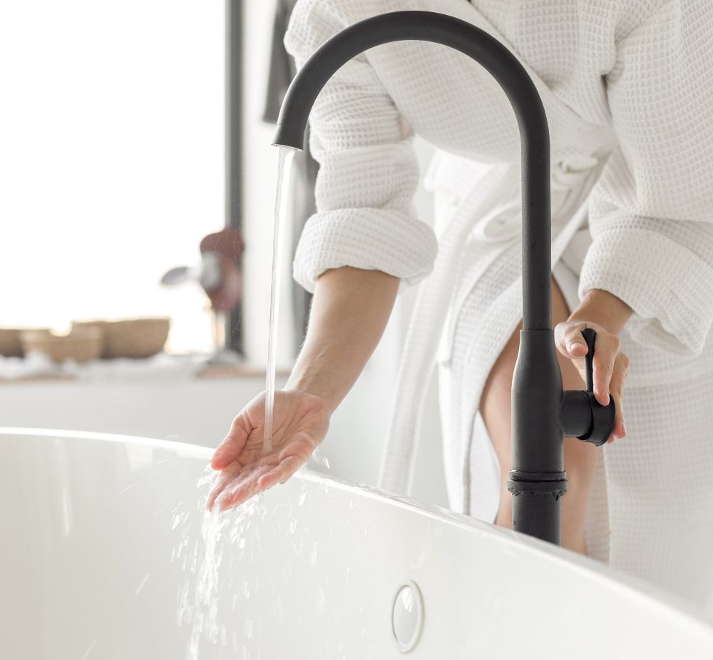 A woman checking the water temperature in the bathtub faucet