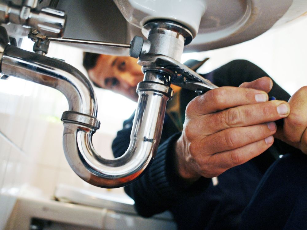 A plumber tightening pipes under a sink