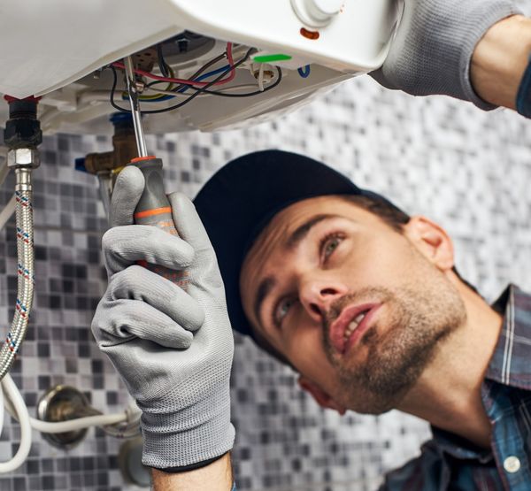 A plumber using a screwdriver to adjust a water heater