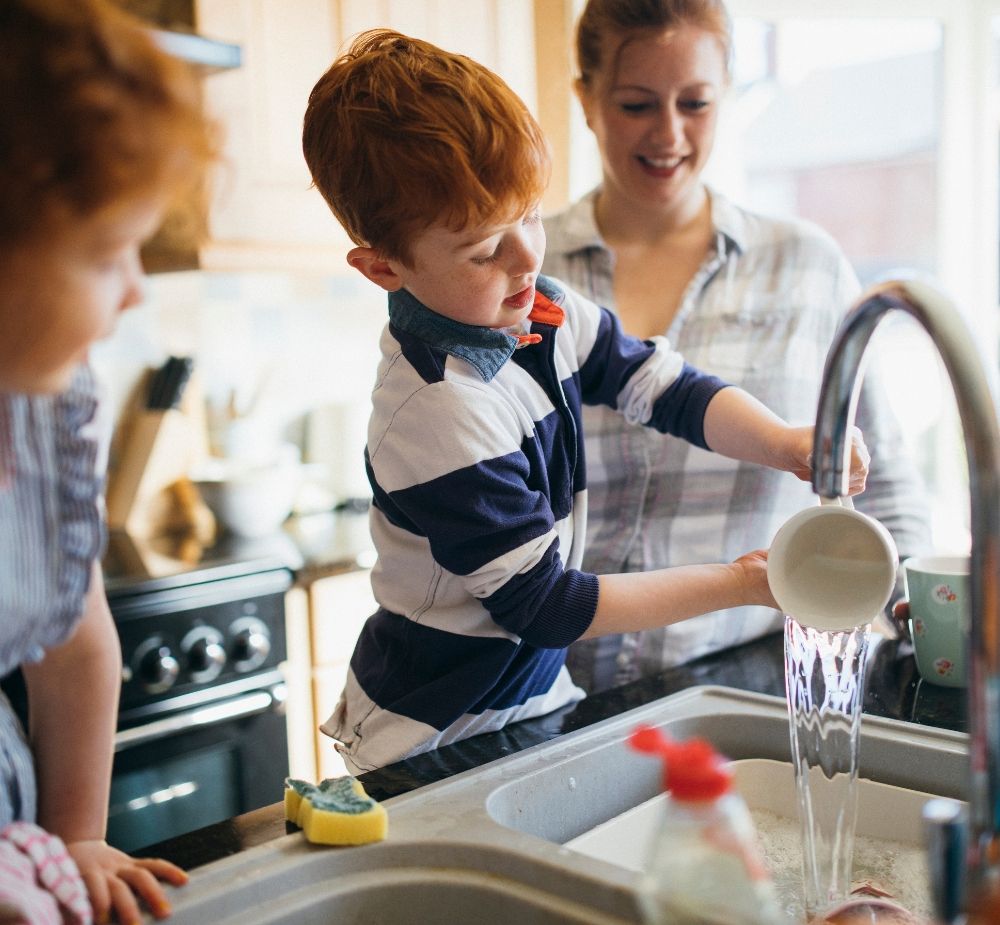 A boy washing dishes with his mother and sister