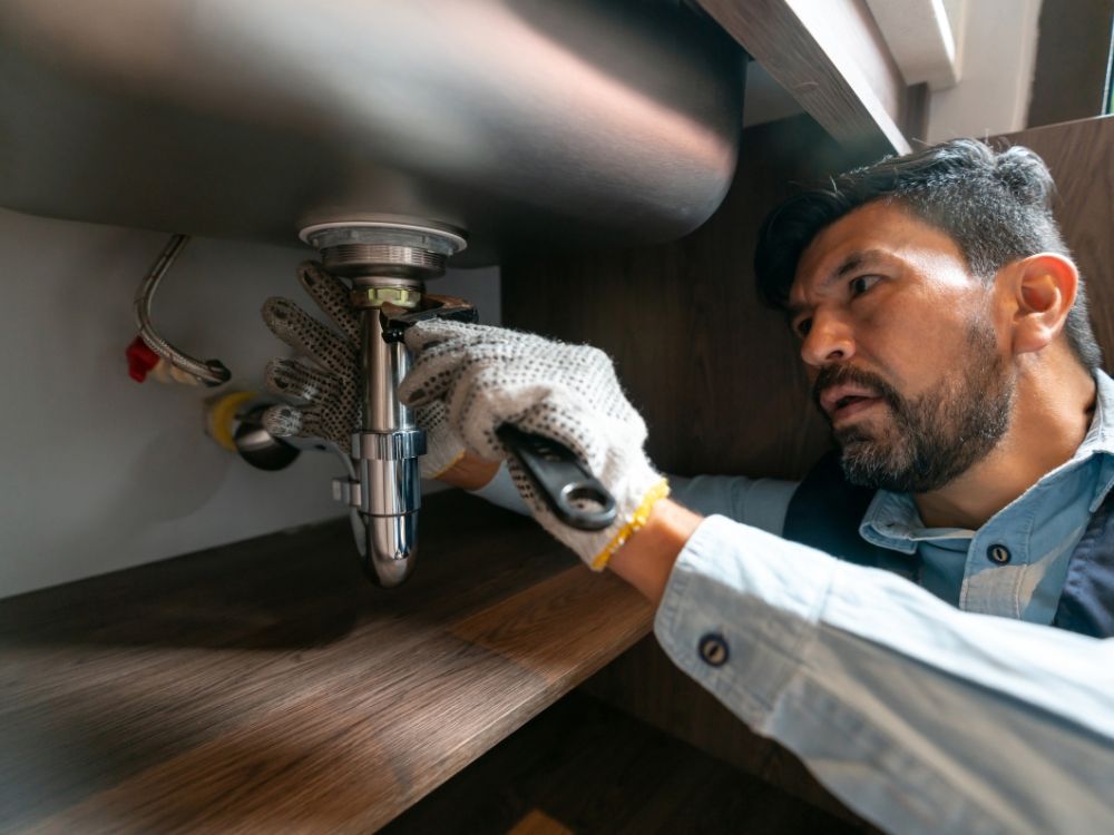 A plumber looking at a pipe under a sink