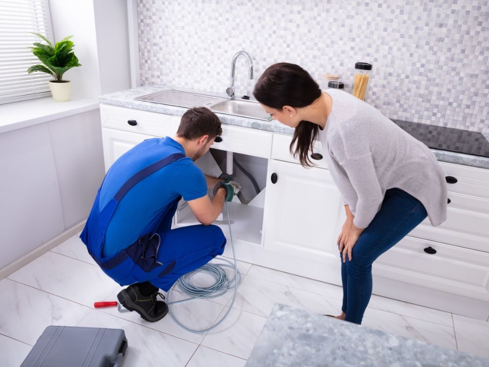 A woman watching a plumber unclog the sink