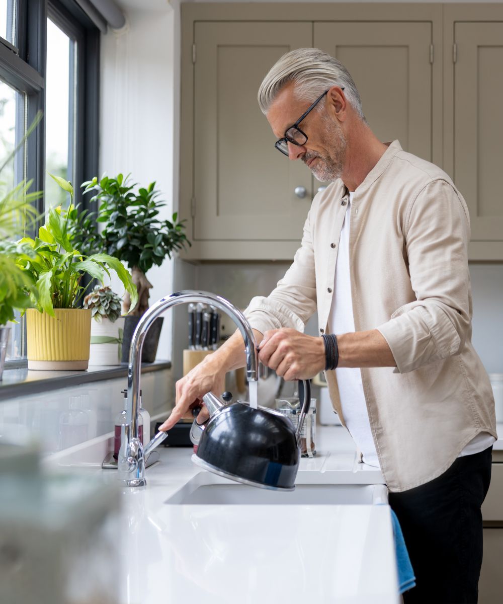 A man getting hot water from the sink to make tea