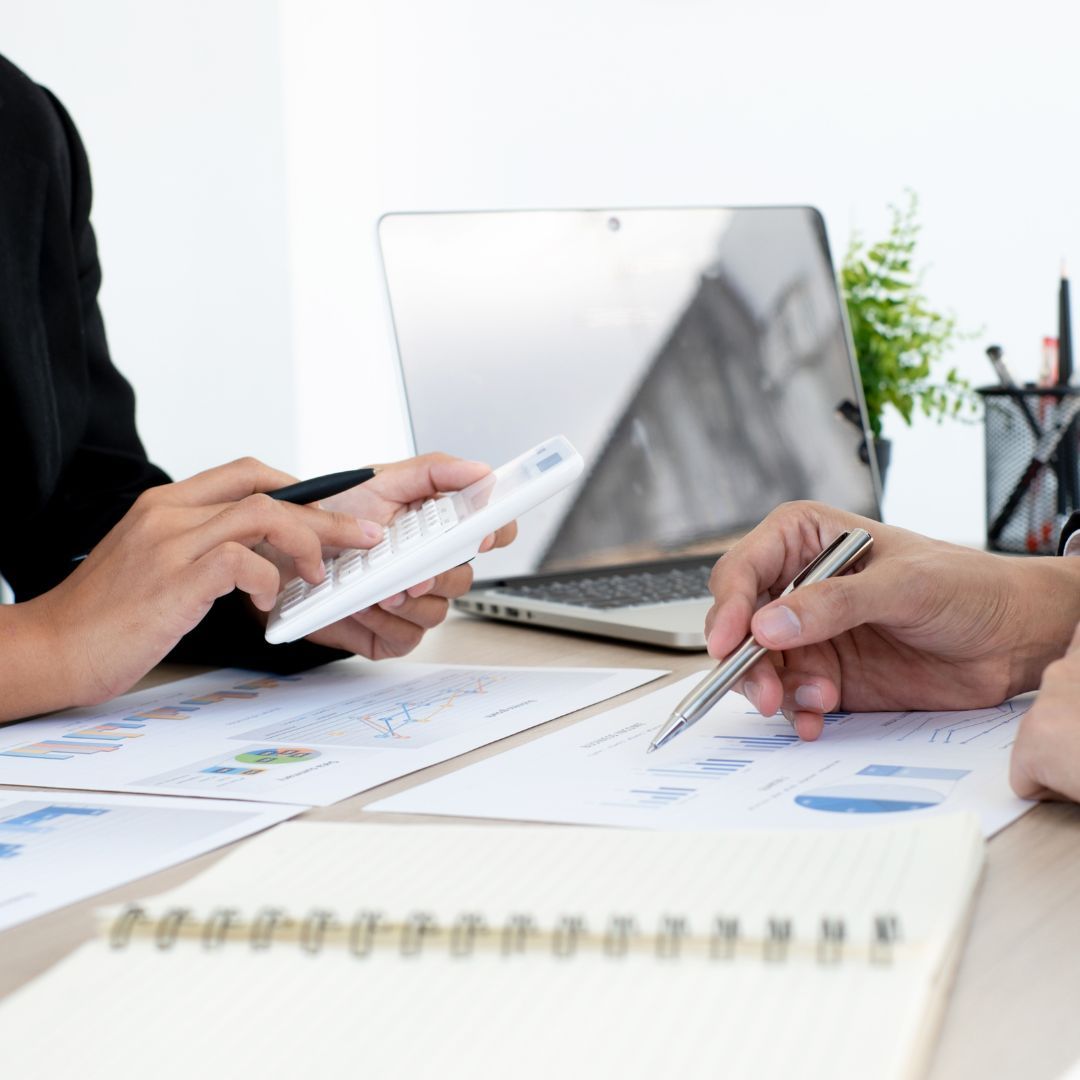 person holding a calculator and another holding a pen over paperwork