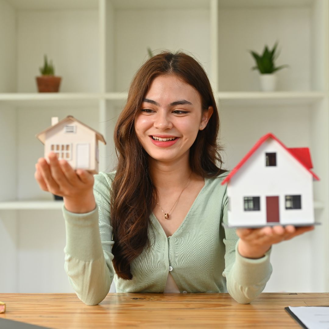 Young adult woman holding two model homes in her hands