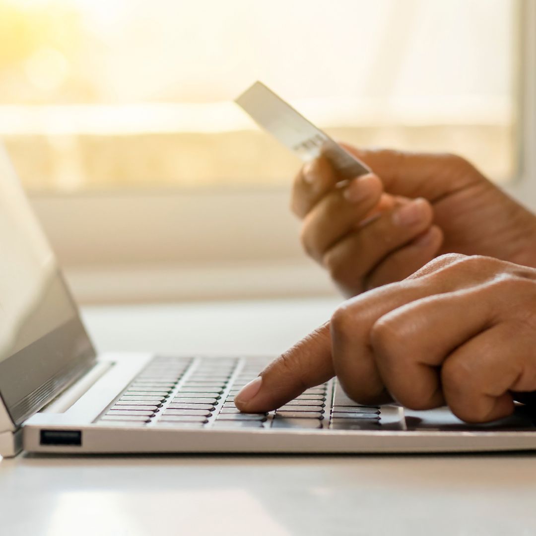 hand holding credit card and other hand typing on computer