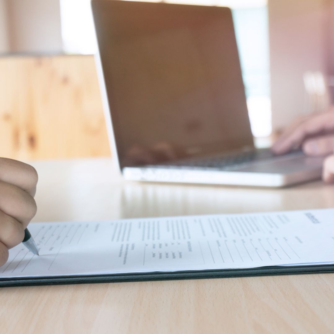 person signing paperwork and a computer