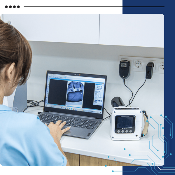 A person in a blue uniform looks at a laptop displaying an X-ray image next to a portable X-ray machine.