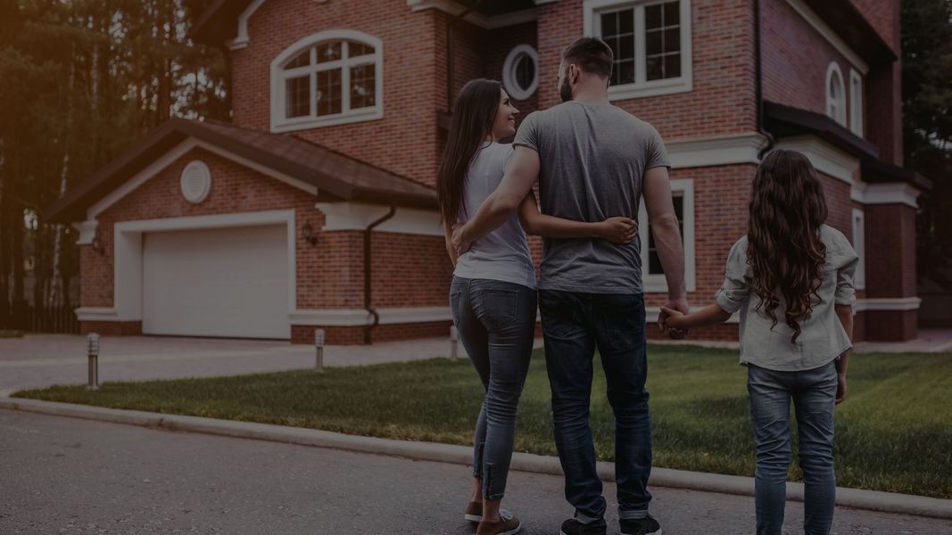 mom and dad hugging and the dad holding a girl's hand while looking at a house. 