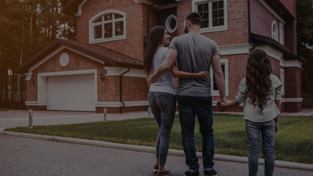 mom and dad hugging and the dad holding a girl's hand while looking at a house. 