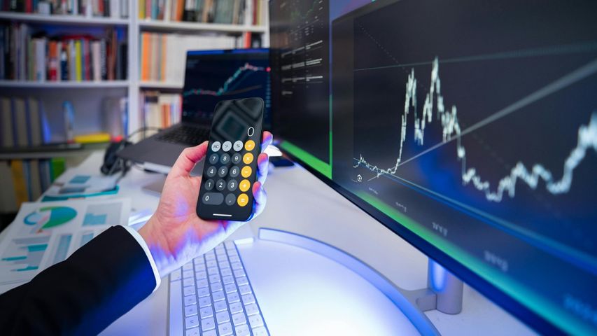 Man holding a calculator while watching graphs