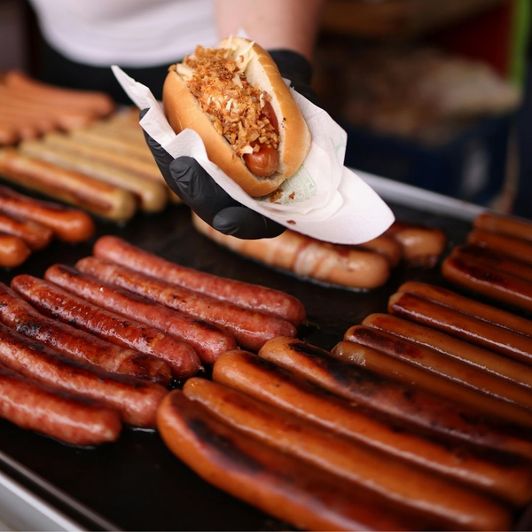 hot dogs on griddle with person holding one in a bun on napkin Make Your Next Event Memorable with Detroit's Finest Hot Dog Trucks 4.jpg