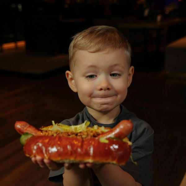 boy holds large hot dog with toppings and smiles Make Your Next Event Memorable with Detroit's Finest Hot Dog Trucks 3.jpg