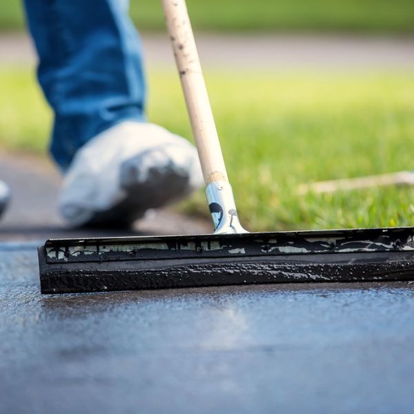 Person applying sealcoating on an asphalt driveway.