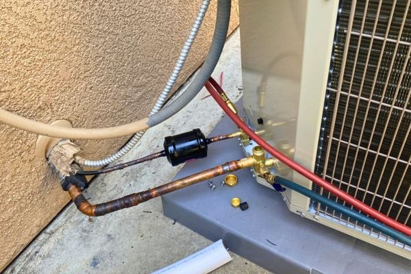 an outdoor HVAC condenser unit with a liquid line filter drier being installed or serviced
