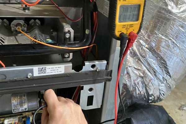 HVAC technician checking the run capacitor on the blower motor using a multimeter/clamp meter