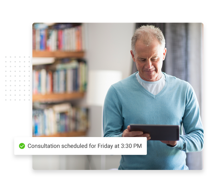 Smiling man looking down at tablet overlaid with a checkmark that says 'Consultation scheduled for Friday at 3:30 PM' Assisted living scheduling software