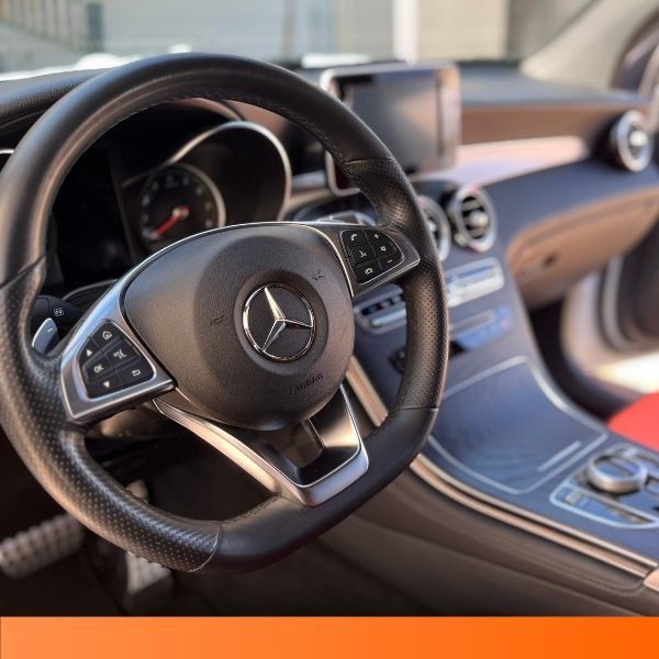 Interior cockpit view of a Mercedes-Benz featuring the steering wheel and console.
