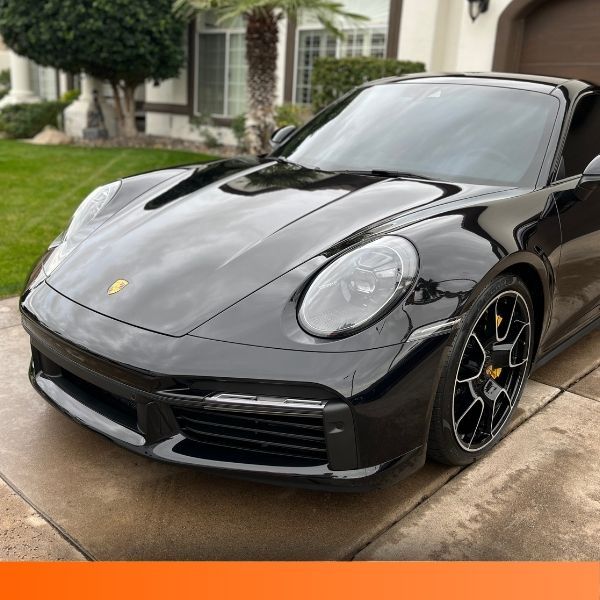 Shiny black Porsche sports car parked in a residential driveway.
