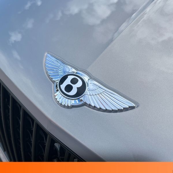 Close-up of the winged 'B' emblem on the hood of a silver Bentley.