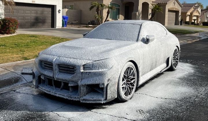 White luxury sedan covered in thick soap foam during a car wash.
