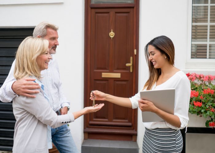 Real Estate agent handing keys to couple in front of house