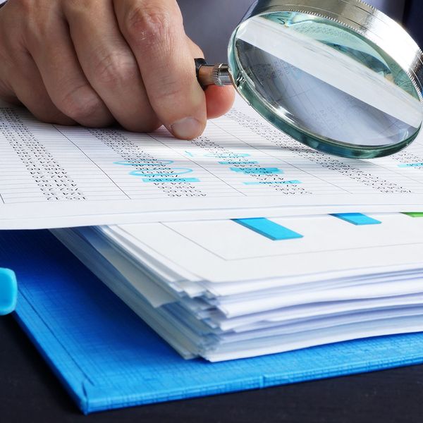 image of a person with a magnifying glass looking over budget reports and spending