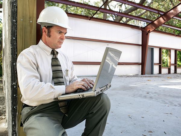 Businessman in a hardhat working on a laptop at the jobsite