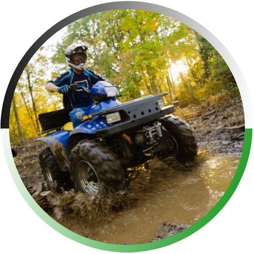 Circular icon of a rider on a blue ATV splashing through a muddy forest trail at sunset.